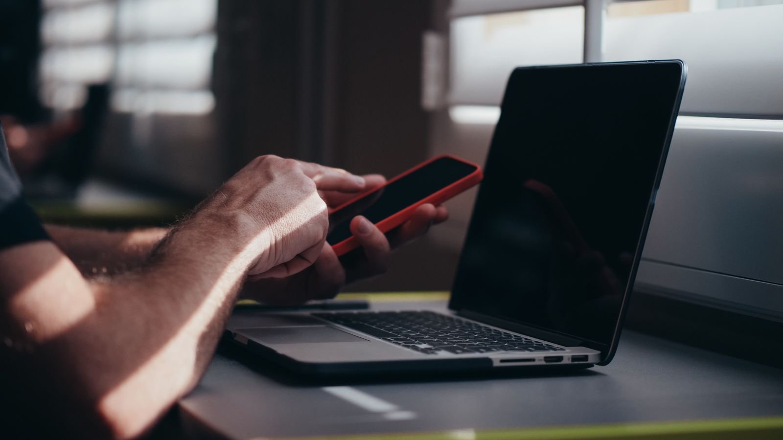 Person using a smartphone in front of a laptop
